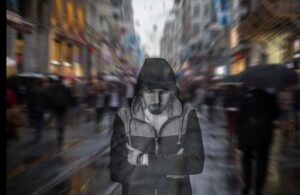 Persona con capucha aislada entre una multitud desenfocada, sobre el sentimiento de no encajar y la soledad