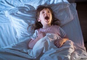 Niña gritando asustada en la cama por la noche, imagen sobre los terrores nocturnos en niños