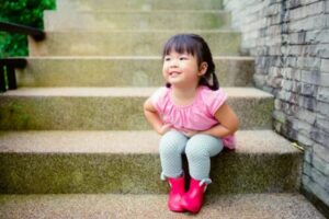 Niña sentada en unas escaleras con gesto de tristeza, sobre la encopresis infantil: síntomas y causas